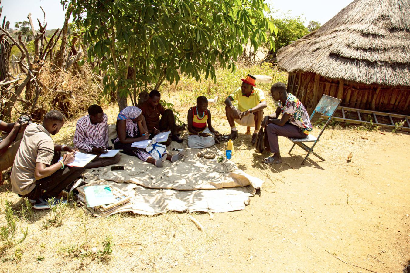 Mitglieder des transdisziplinären Forschungsteams der Makerere-Universität und des Uganda National Museum bei der Feldarbeit in Kaabong, im Nordosten von Uganda. Sie sprechen mit einer lokalen Heilerin und Heilpflanzenkundigen der Ik über deren Heilpflanzenwissen. Dazu arbeiten sie mit einem Übersetzer.